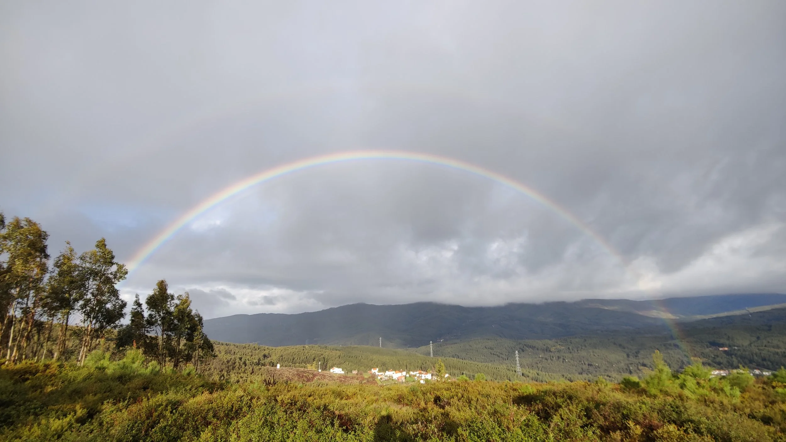 A rainbow arching over a forested mountain valley in Portugal